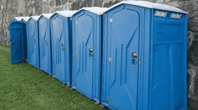Row of blue portable toilets lined up on grass against a stone wall for event sanitation in Minneapolis, MN