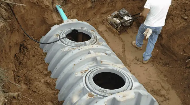 Septic tank installation showing a technician compacting soil around a new poly septic tank in an excavation pit in Minneapolis, MN